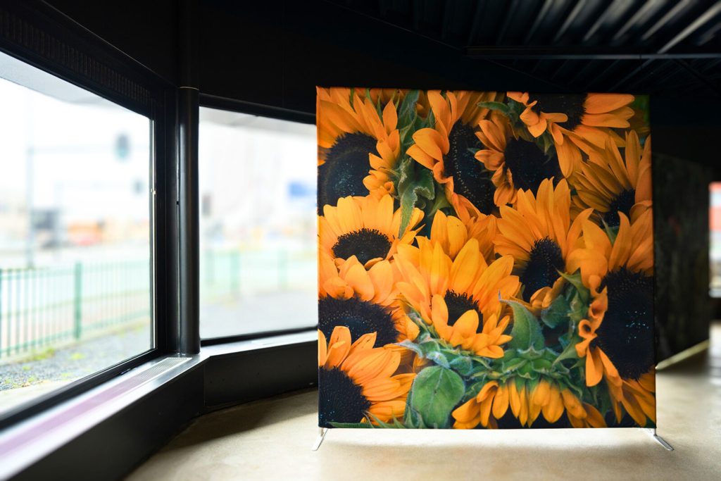 Een beurswand van zonnebloemen in een moderne, donkere ruimte met grote ramen aan de linkerzijde die uitkijken op straat.